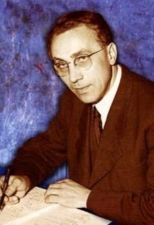 Olav Valen-Sendstad. Mies lasien kanssa istuu pöydän ääressä, sininen tausta, ruskea puku ja valkoinen kaulus.